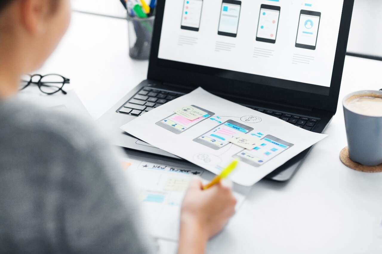 Designer ved skrivebord med digitale skisser og brukergrensesnitt – symbol for verdiskaping gjennom teknologi